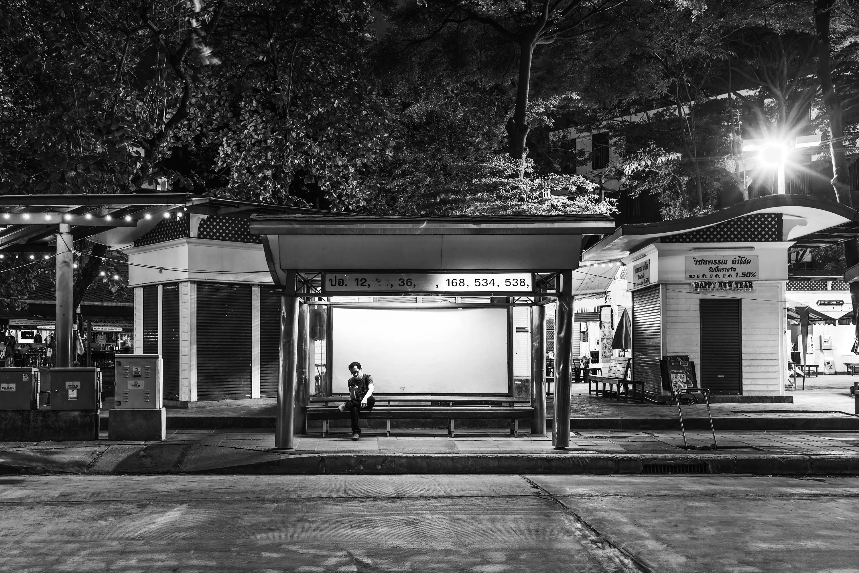 Beacon
The Sea #13

// The inception of the Beacon series traces back to a solitary photograph captured for the project "Portuguese Sea" by Bernardo Caria. Rooted in Fernando Pessoa's 1922 poem of the same title, the project delves into diverse interpretations of home. At its core, the sea symbolizes a wellspring of inspiration, exploration, and identity.

A year later, the poetic essence of Pessoa's verses metamorphosed into a lens-based art series titled Beacon. The expansive sea embodies boundlessness and promise, a stark contrast to the confines of urban living, particularly within sprawling megacities. Amidst the bustling metropolis, where individuals often feel lost amidst concrete canyons and a cacophony of noise, finding the tranquility Pessoa seeks in the sea proves elusive.

Yet, within the urban labyrinth, a languid light unveils the unseen and overlooked. Neon emanates from forsaken bus stop billboards, casting an ethereal glow reminiscent of coastal beacons. This luminous voyage through the cityscape evokes the hues of the sea—rugged and brilliant, evoking a longing for home. The tales of those setting out on their journeys remain shrouded in mystery to us; we merely glimpse them as they wait or vanish into the distance. It's only the illumination of the bus stop that hints at a narrative, leaving us to conjure the story within our imaginations.

Adding another layer to the series, documenting the fading Bangkok bus stops adorned with colossal backlit advertisements becomes a testament to identity and transition. As 2024 unfolds, these iconic structures are gradually supplanted by more economical and utilitarian counterparts, signaling an era's end.

At the core of the Beacon series lies photography, offering a distinctive 360º narrative journey that encompasses different media, presented in three parts - The Coast (mixed media), The Sea (photography), and The Wave (collectors reward airdrops) for, “Narratiff” with Colonna Contemporary.