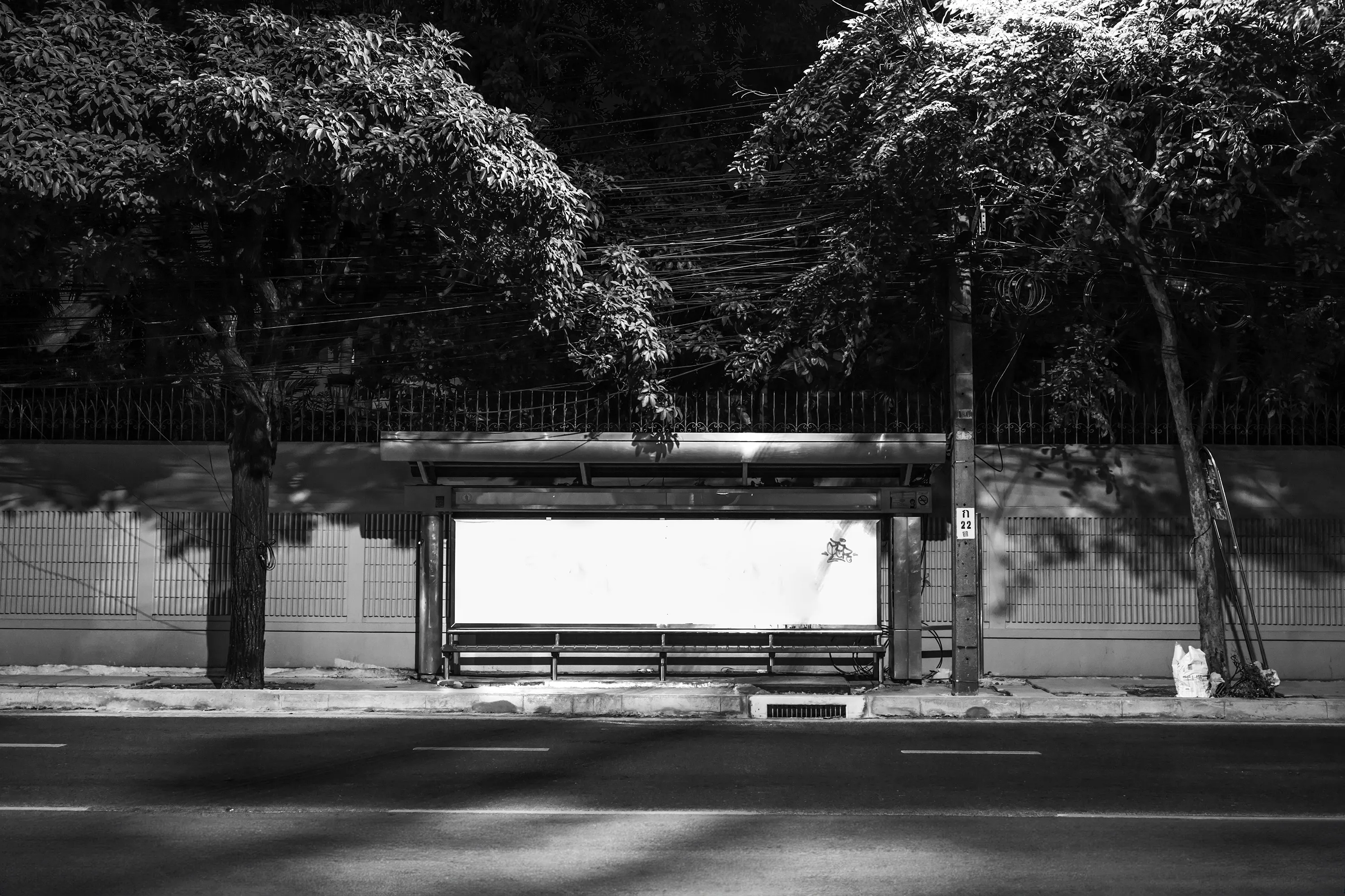 Beacon
The Sea #01

The photograph is paired with a signed 29 x 20 cm single edition fine art print on Enhanced Matte Paper 230g using archival pigment ink, and a garland commonly hung on the mirror by bus drivers.

// The inception of the Beacon series traces back to a solitary photograph captured for the project "Portuguese Sea" by Bernardo Caria. Rooted in Fernando Pessoa's 1922 poem of the same title, the project delves into diverse interpretations of home. At its core, the sea symbolizes a wellspring of inspiration, exploration, and identity.

A year later, the poetic essence of Pessoa's verses metamorphosed into a lens-based art series titled Beacon. The expansive sea embodies boundlessness and promise, a stark contrast to the confines of urban living, particularly within sprawling megacities. Amidst the bustling metropolis, where individuals often feel lost amidst concrete canyons and a cacophony of noise, finding the tranquility Pessoa seeks in the sea proves elusive.

Yet, within the urban labyrinth, a languid light unveils the unseen and overlooked. Neon emanates from forsaken bus stop billboards, casting an ethereal glow reminiscent of coastal beacons. This luminous voyage through the cityscape evokes the hues of the sea—rugged and brilliant, evoking a longing for home. The tales of those setting out on their journeys remain shrouded in mystery to us; we merely glimpse them as they wait or vanish into the distance. It's only the illumination of the bus stop that hints at a narrative, leaving us to conjure the story within our imaginations.

Adding another layer to the series, documenting the fading Bangkok bus stops adorned with colossal backlit advertisements becomes a testament to identity and transition. As 2024 unfolds, these iconic structures are gradually supplanted by more economical and utilitarian counterparts, signaling an era's end.

At the core of the Beacon series lies photography, offering a distinctive 360º narrative journey that encompasses different media, presented in three parts - The Coast (mixed media), The Sea (photography), and The Wave (collectors reward airdrops) for, “Narratiff” with Colonna Contemporary.