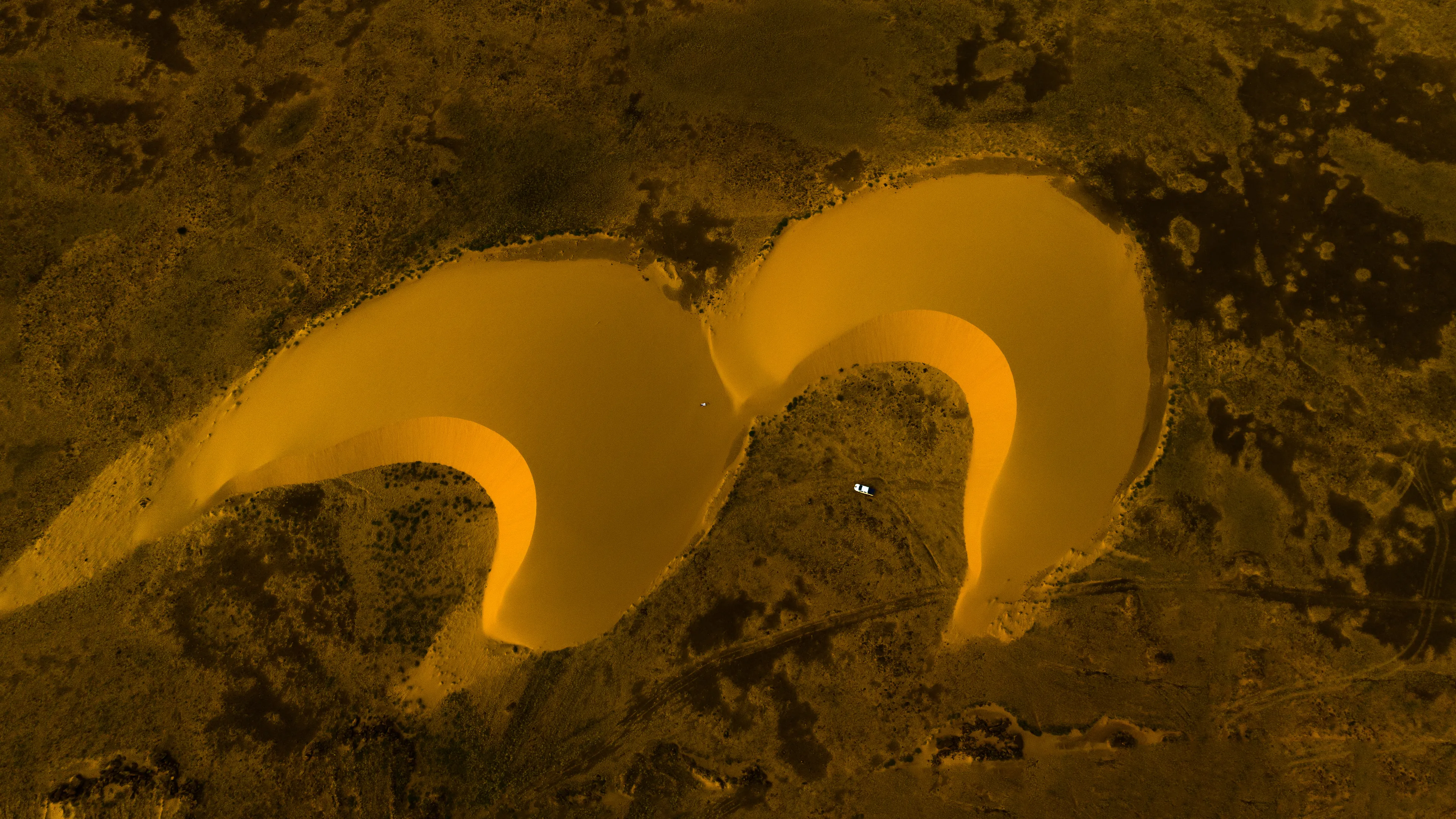 The light gently touches the tips of the twin barchan dunes. As I cross the desert, I am always fascinated by these dunes, especially when they form on contrasting surfaces. These two dunes act like quotation marks between the green and arid ground, creating a perfect surreal composition.