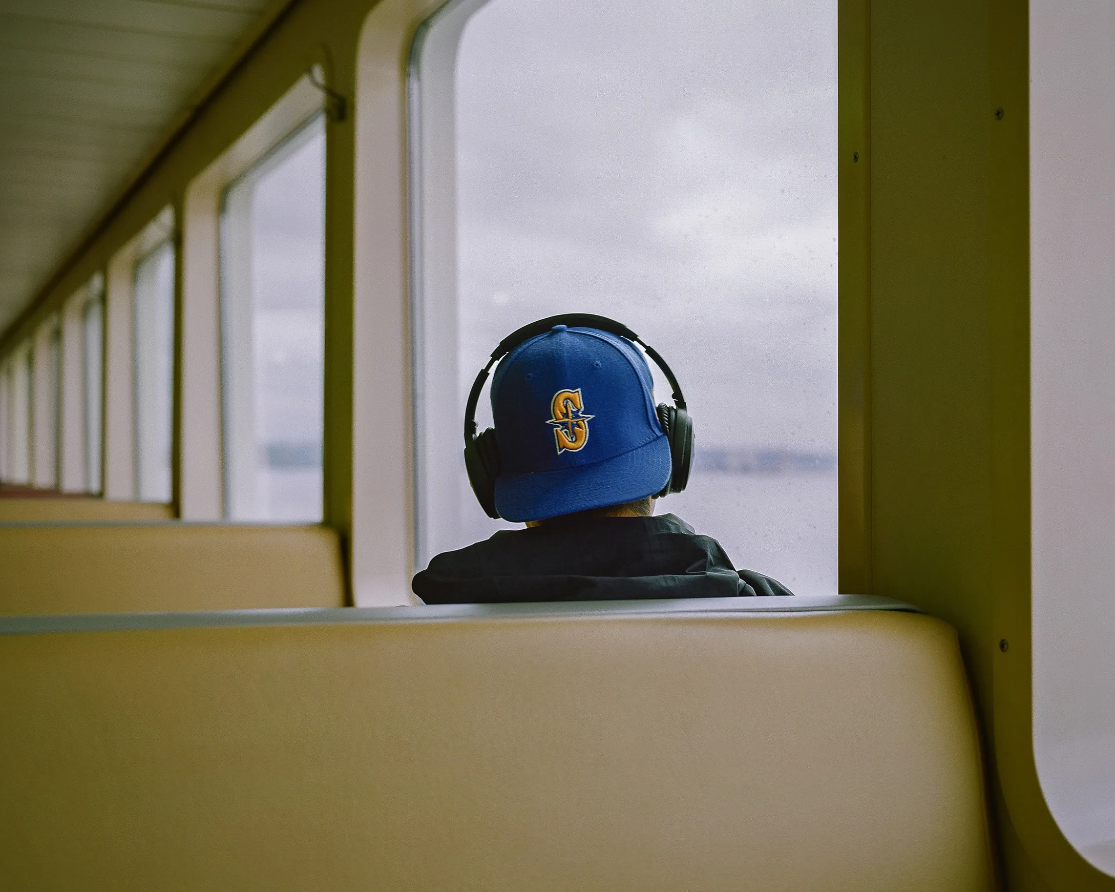Growing up, I always looked forward to watching the Major League Baseball home run derby every summer. One player that always stood out to me was Ken Griffey Jr, with his beautiful swing and signature backwards Seattle Mariners hat.

One day, as I was exploring on the ferry shooting some photos, I came across a passenger sitting with headphones on over a backwards throwback Mariners hat, looking out through the rain drops on the window to his right. Seeing the throwback hat immediately took me back to those youthful summer days, admiring Ken Griffey Jr. on television.

It doesn’t get much more “Seattle” than this. 
Please enjoy, “Throwback”.