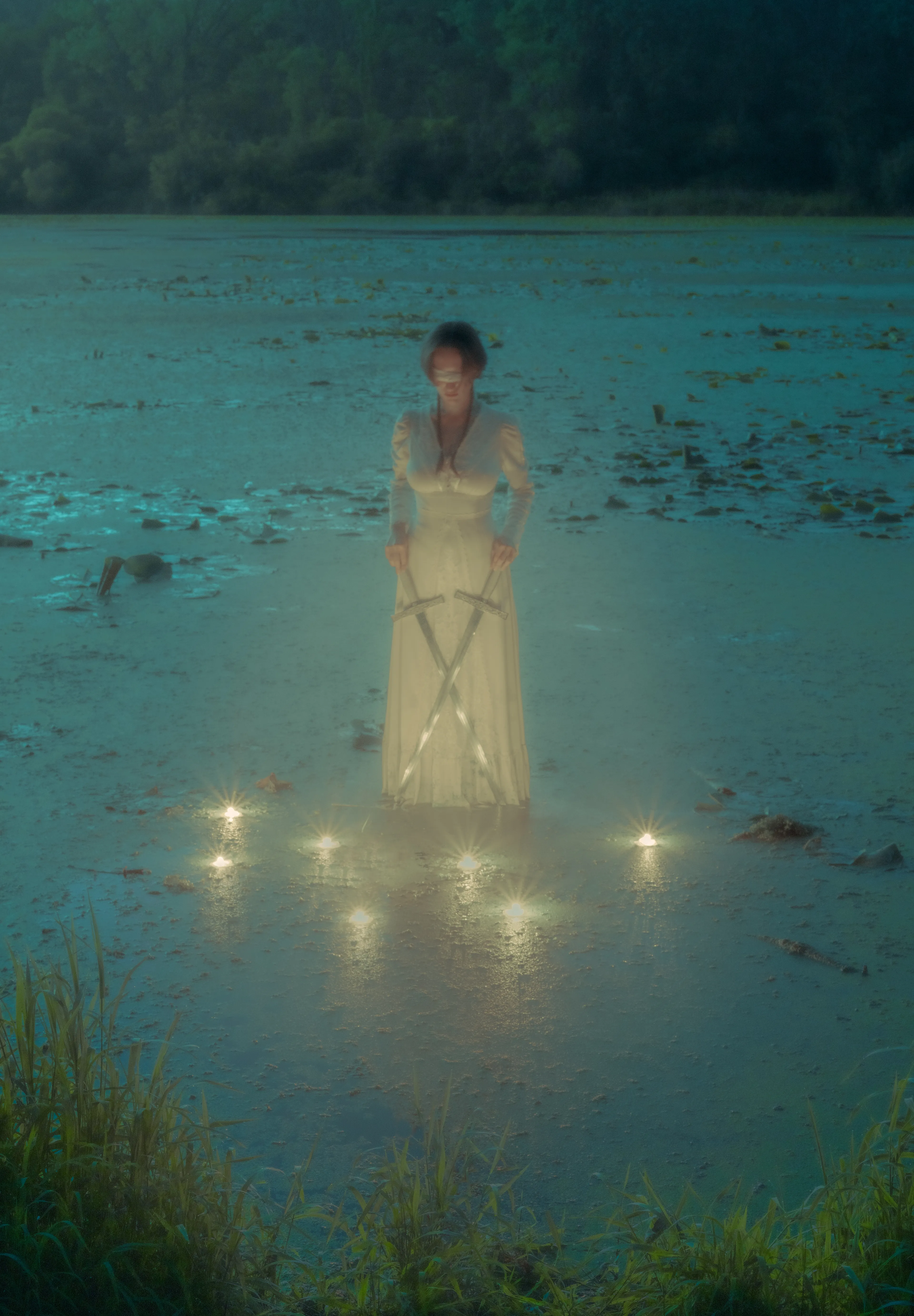 Upright: Taking the time to make tough choice wisely, balancing perspectives, trusting the intuition, using  intellect, allowing things to grow before moving too quickly 

Reversed: Impossible decision, becoming stagnant, inability to see past one’s own emotions, neglect, losing one’s self to overgrowth or decay 

A woman stands like a statue on the waters of a swampy lake. At her feet she holds two swords pointing opposite directions. Blindfolded, her gaze aims downwards toward the soft light of seven candles floating with her in the water. 

The swamp has long been considered a viscous place, not suitable for the building and farming required for human comfort. The swamp, characterized by its molding stillness, is also an entity of inherent change. In some regions, it comes and goes with the seasons, but in all swamps there is abundant life in a constant shimmering kaleidoscope of overlapping biodiversity. 

The woman here has a choice to make, a difficult one. Blindfolded, the situation before her is unclear. She is only guided by the vague lights of the seven candles before her. The swords are her intellect, the water her emotions. She must wield both the power of her mind and intuition to make the right choice. Making the choice too soon, she risks not reaping the full benefits of a matured thought process. Taking too long, she risks her options outgrowing her abilities and withering with time. 

Though a decision may seem black or white, keep in mind that there are almost always more paths than it seems. Consider the number seven: the sum of the spiritual number three and material number four. Seven, a prime number. Seven, the number of notes in a scale, the number of days in a week, the number of colors in the rainbow and number of deadly sins. The moon phases last approximately seven days, and a woman’s hormonal cycle follows suit. Seven, the number of variety, distinction, change and abundance. Seven cannot be divided by two, one must remain. 