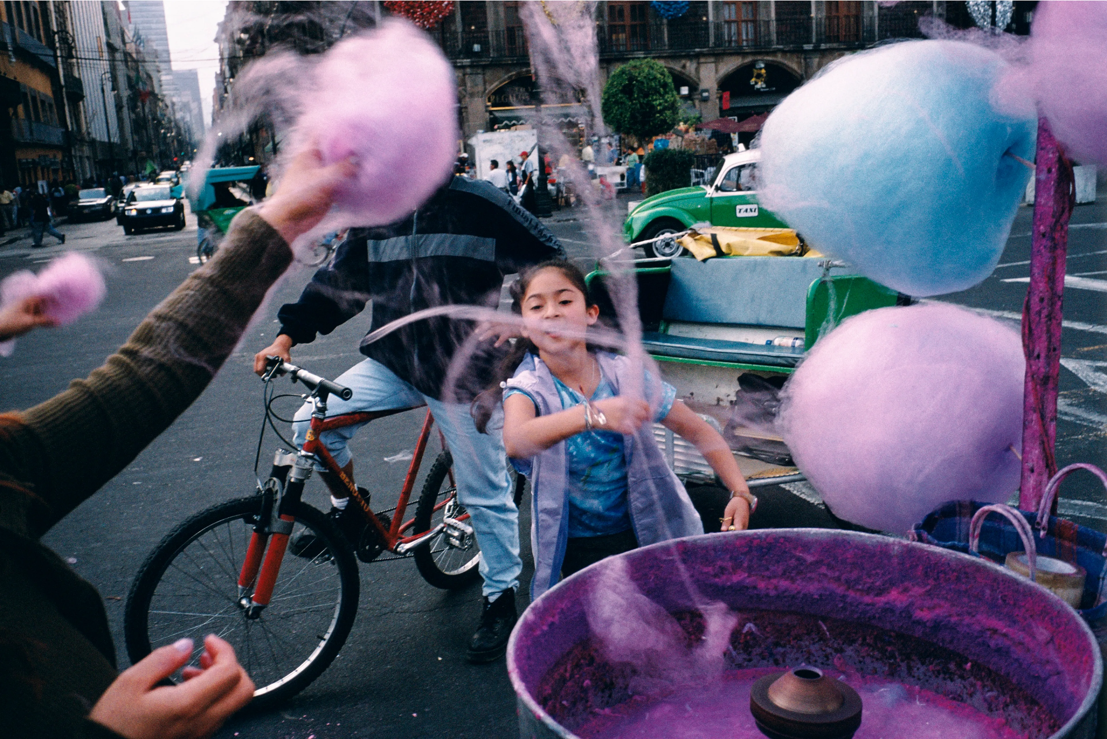 From his first visit in 1975, he was immediately captivated by the vibrant life in the streets of Mexico. While his early black and white photos often feature stark, striking graphics, his foray into color photography starting in 1978—inspired by the light and color of the Mexican streets—marks a turning point in his work.

Throughout his work from Mexico, his rich compositions create compelling visual complexity—‘La Calle’ features strong, saturated colors, which evoke haunting, enigmatic scenes of the everyday. “I work extremely intuitively. I wander, I respond,” he says. “Am I aware of certain elements rationally at times? Sure. But I think that often when I am more aware of them, it usually means that the picture falls flat.”

Webb somehow manages to capture these surprising scenes, which add an otherworldly poetry to the genre of street photography.