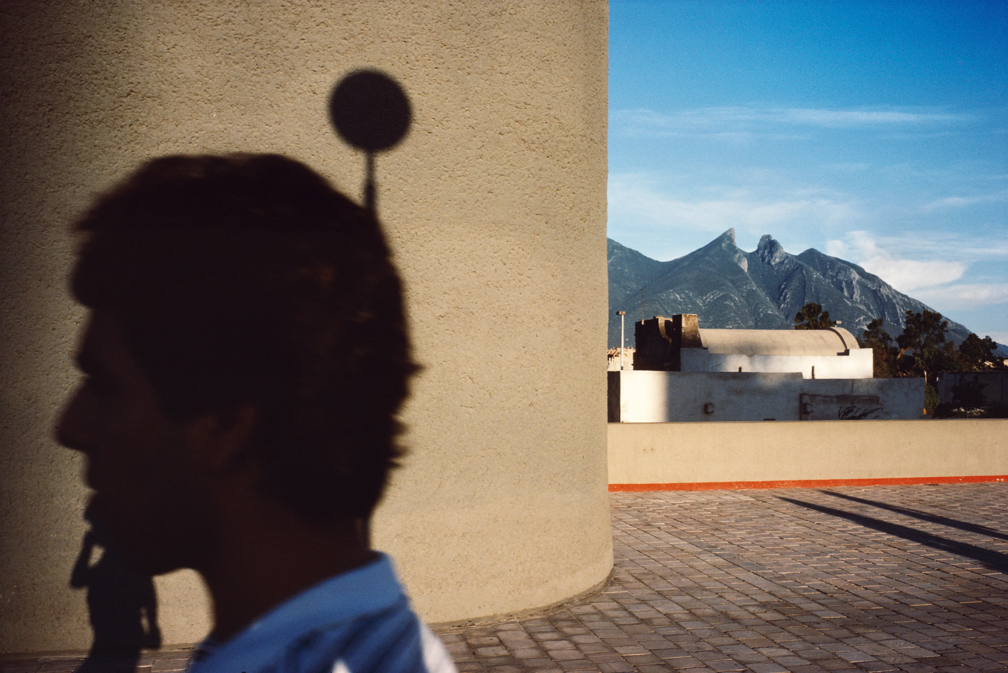 From his first visit in 1975, he was immediately captivated by the vibrant life in the streets of Mexico. While his early black and white photos often feature stark, striking graphics, his foray into color photography starting in 1978—inspired by the light and color of the Mexican streets—marks a turning point in his work.

Throughout his work from Mexico, his rich compositions create compelling visual complexity—‘La Calle’ features strong, saturated colors, which evoke haunting, enigmatic scenes of the everyday. “I work extremely intuitively. I wander, I respond,” he says. “Am I aware of certain elements rationally at times? Sure. But I think that often when I am more aware of them, it usually means that the picture falls flat.”

Webb somehow manages to capture these surprising scenes, which add an otherworldly poetry to the genre of street photography.