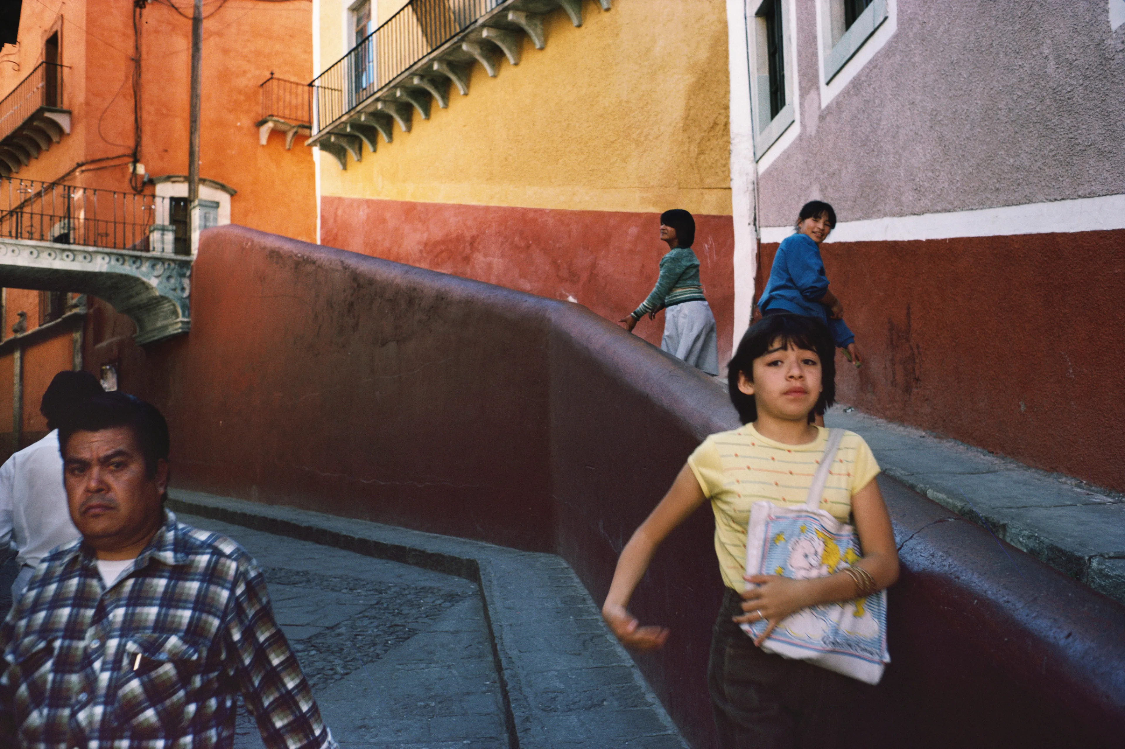 From his first visit in 1975, he was immediately captivated by the vibrant life in the streets of Mexico. While his early black and white photos often feature stark, striking graphics, his foray into color photography starting in 1978—inspired by the light and color of the Mexican streets—marks a turning point in his work.

Throughout his work from Mexico, his rich compositions create compelling visual complexity—‘La Calle’ features strong, saturated colors, which evoke haunting, enigmatic scenes of the everyday. “I work extremely intuitively. I wander, I respond,” he says. “Am I aware of certain elements rationally at times? Sure. But I think that often when I am more aware of them, it usually means that the picture falls flat.”

Webb somehow manages to capture these surprising scenes, which add an otherworldly poetry to the genre of street photography.