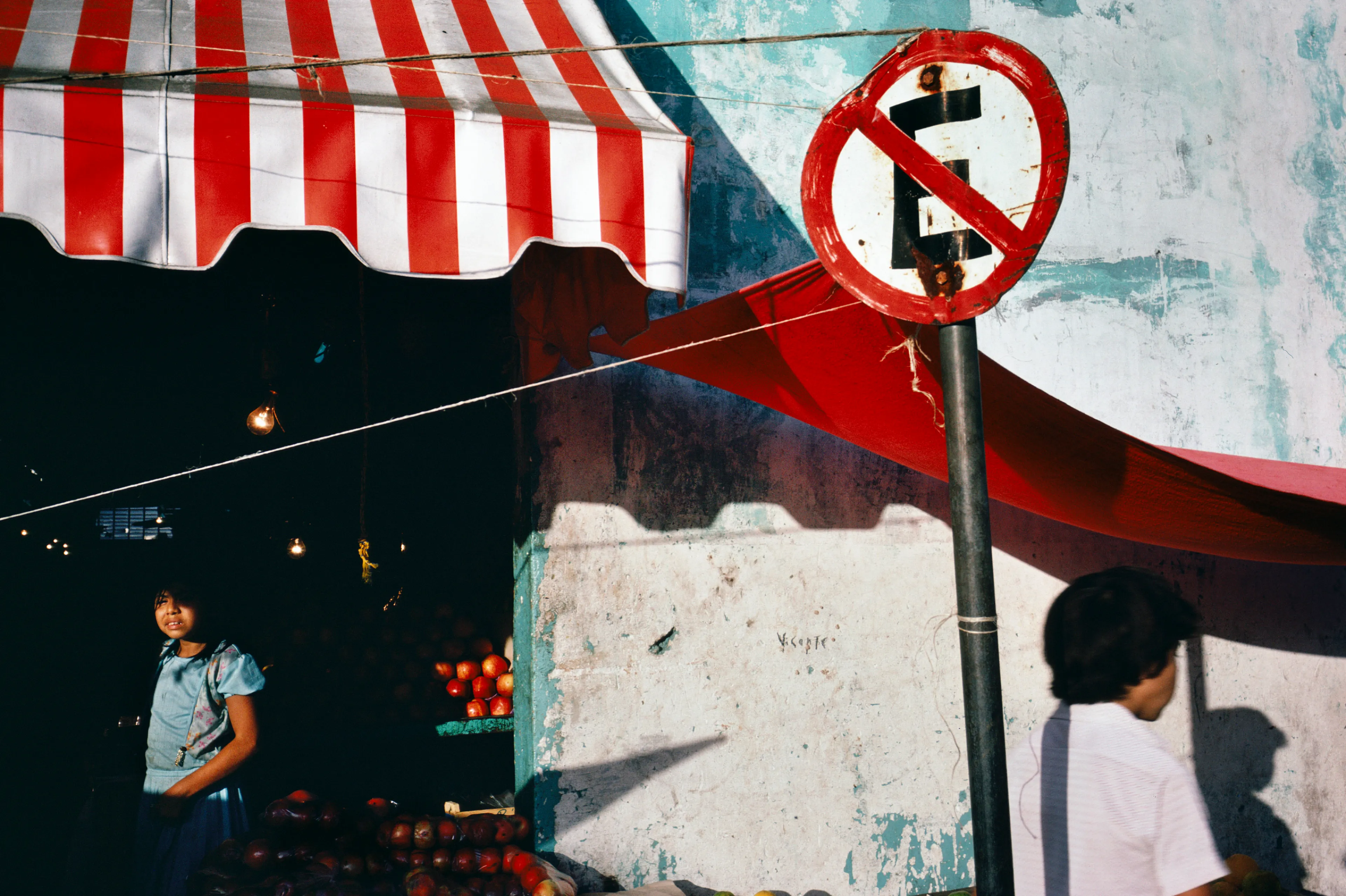 From his first visit in 1975, he was immediately captivated by the vibrant life in the streets of Mexico. While his early black and white photos often feature stark, striking graphics, his foray into color photography starting in 1978—inspired by the light and color of the Mexican streets—marks a turning point in his work.

Throughout his work from Mexico, his rich compositions create compelling visual complexity—‘La Calle’ features strong, saturated colors, which evoke haunting, enigmatic scenes of the everyday. “I work extremely intuitively. I wander, I respond,” he says. “Am I aware of certain elements rationally at times? Sure. But I think that often when I am more aware of them, it usually means that the picture falls flat.”

Webb somehow manages to capture these surprising scenes, which add an otherworldly poetry to the genre of street photography.