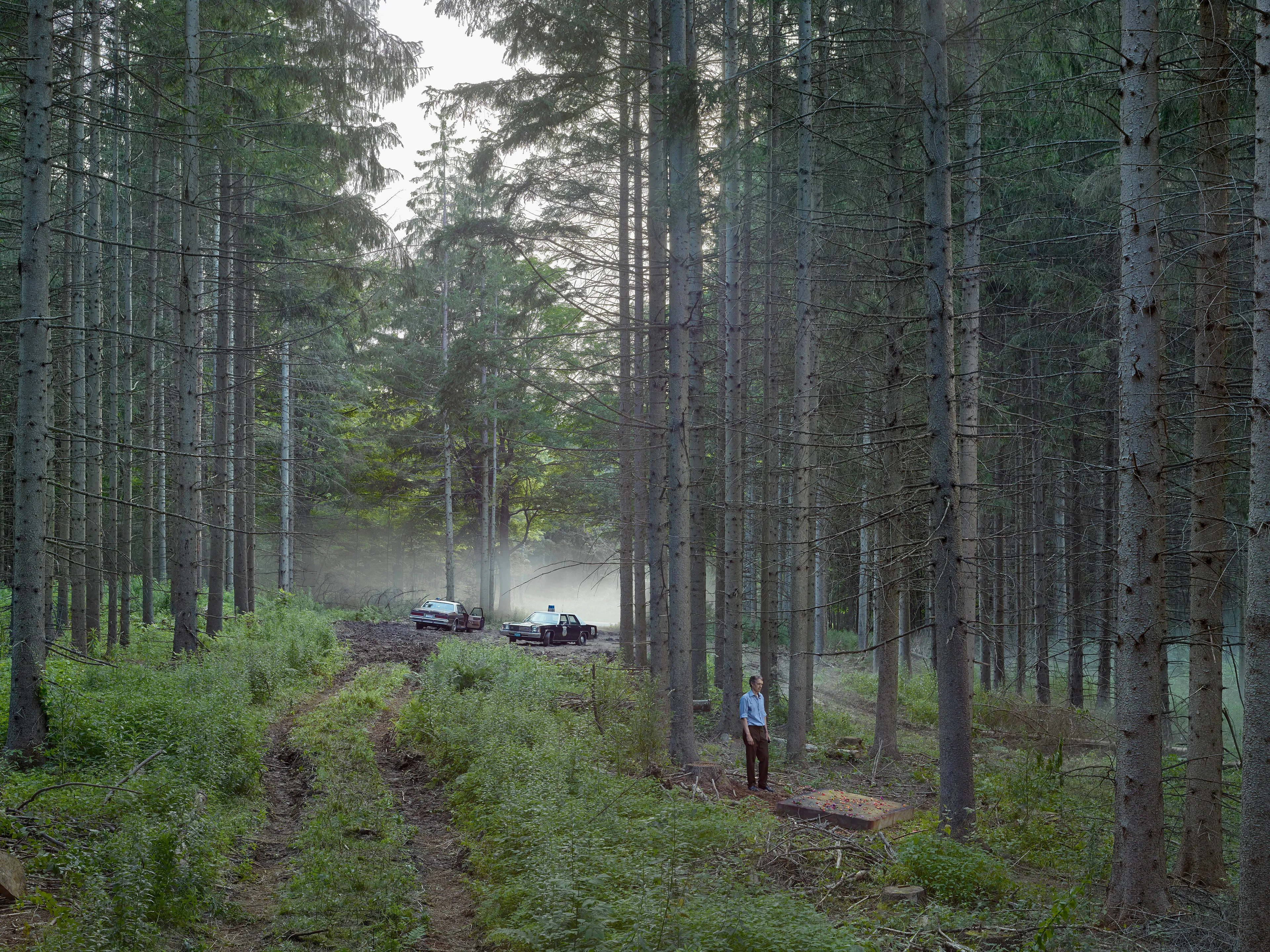 Cathedral of the Pines (2013-14) was produced in the rural woodlands surrounding Becket, Massachusetts, a small town that was first settled in 1740 and home to the titular forest trail the work is named after. There’s a pervasive stillness that exists in the works of this collection. As we viewers tour these pictures, we find the quietude of the cabins and forest landscapes become hosts to a dark and meditative dwelling of the subjects that populate these places. As with much of Crewdson’s work, the loneliness and alienation of his subjects are deeply pronounced, and the cool blue and green hues that saturate the frames characterize the emotional content to pair with the unusual encounters received by their viewers.

While the domestic interior scenes extend a trademark narrative form that the photographer is widely recognized for, Crewdson’s landscape scenes enrichen the series by taking inspiration from 19th century American landscape painting. The compositional exactitudes and ornate geometries the photographer employs contextualize his images in the framework of classical tradition. Cathedral of the Pines thus becomes an update to the legacy of ‘Americana’, and a revisionist practice which sees the lores of American ideals become overtaken with the internal disturbances of its unwell occupants.

Edition: 1 of 1