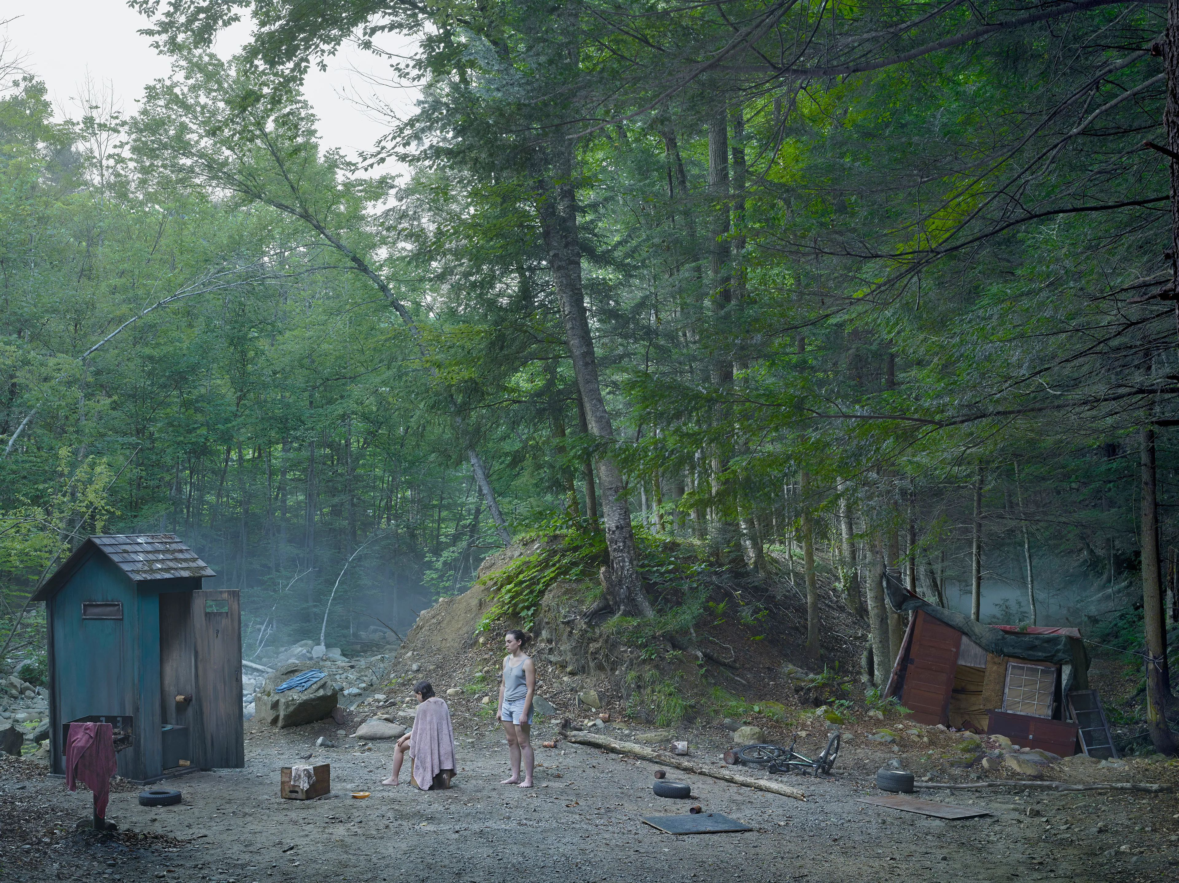 Cathedral of the Pines (2013-14) was produced in the rural woodlands surrounding Becket, Massachusetts, a small town that was first settled in 1740 and home to the titular forest trail the work is named after. There’s a pervasive stillness that exists in the works of this collection. As we viewers tour these pictures, we find the quietude of the cabins and forest landscapes become hosts to a dark and meditative dwelling of the subjects that populate these places. As with much of Crewdson’s work, the loneliness and alienation of his subjects are deeply pronounced, and the cool blue and green hues that saturate the frames characterize the emotional content to pair with the unusual encounters received by their viewers.

While the domestic interior scenes extend a trademark narrative form that the photographer is widely recognized for, Crewdson’s landscape scenes enrichen the series by taking inspiration from 19th century American landscape painting. The compositional exactitudes and ornate geometries the photographer employs contextualize his images in the framework of classical tradition. Cathedral of the Pines thus becomes an update to the legacy of ‘Americana’, and a revisionist practice which sees the lores of American ideals become overtaken with the internal disturbances of its unwell occupants.

Edition: 1 of 1