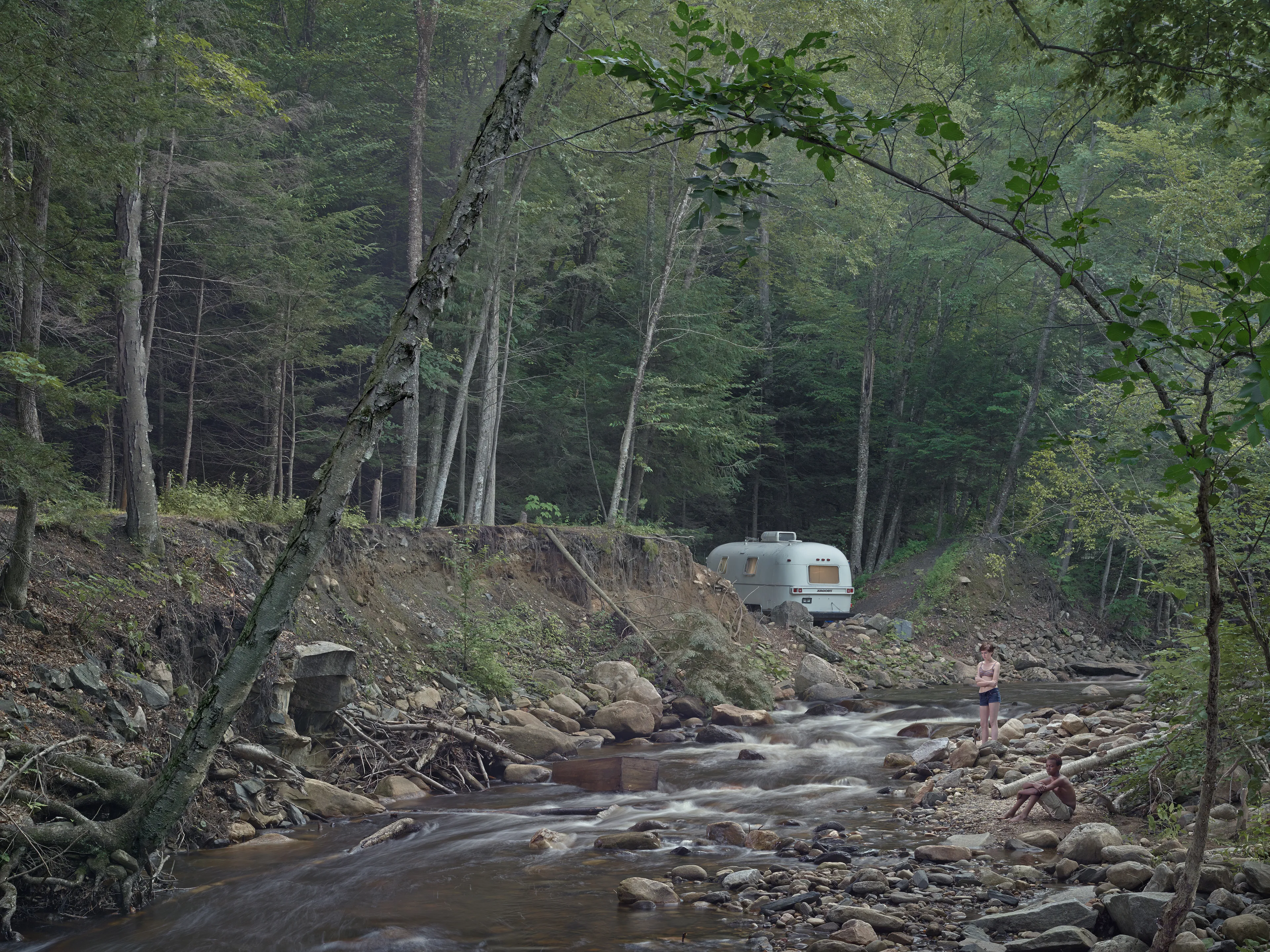 Cathedral of the Pines (2013-14) was produced in the rural woodlands surrounding Becket, Massachusetts, a small town that was first settled in 1740 and home to the titular forest trail the work is named after. There’s a pervasive stillness that exists in the works of this collection. As we viewers tour these pictures, we find the quietude of the cabins and forest landscapes become hosts to a dark and meditative dwelling of the subjects that populate these places. As with much of Crewdson’s work, the loneliness and alienation of his subjects are deeply pronounced, and the cool blue and green hues that saturate the frames characterize the emotional content to pair with the unusual encounters received by their viewers.

While the domestic interior scenes extend a trademark narrative form that the photographer is widely recognized for, Crewdson’s landscape scenes enrichen the series by taking inspiration from 19th century American landscape painting. The compositional exactitudes and ornate geometries the photographer employs contextualize his images in the framework of classical tradition. Cathedral of the Pines thus becomes an update to the legacy of ‘Americana’, and a revisionist practice which sees the lores of American ideals become overtaken with the internal disturbances of its unwell occupants.

Edition: 1 of 1