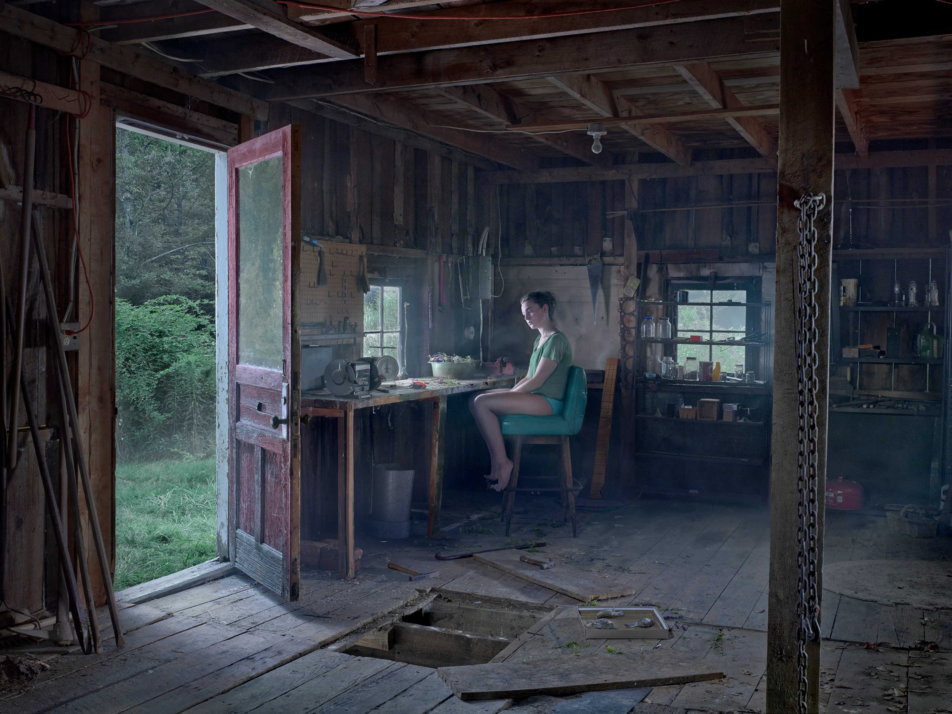 Cathedral of the Pines (2013-14) was produced in the rural woodlands surrounding Becket, Massachusetts, a small town that was first settled in 1740 and home to the titular forest trail the work is named after. There’s a pervasive stillness that exists in the works of this collection. As we viewers tour these pictures, we find the quietude of the cabins and forest landscapes become hosts to a dark and meditative dwelling of the subjects that populate these places. As with much of Crewdson’s work, the loneliness and alienation of his subjects are deeply pronounced, and the cool blue and green hues that saturate the frames characterize the emotional content to pair with the unusual encounters received by their viewers.

While the domestic interior scenes extend a trademark narrative form that the photographer is widely recognized for, Crewdson’s landscape scenes enrichen the series by taking inspiration from 19th century American landscape painting. The compositional exactitudes and ornate geometries the photographer employs contextualize his images in the framework of classical tradition. Cathedral of the Pines thus becomes an update to the legacy of ‘Americana’, and a revisionist practice which sees the lores of American ideals become overtaken with the internal disturbances of its unwell occupants.

Edition: 1 of 1