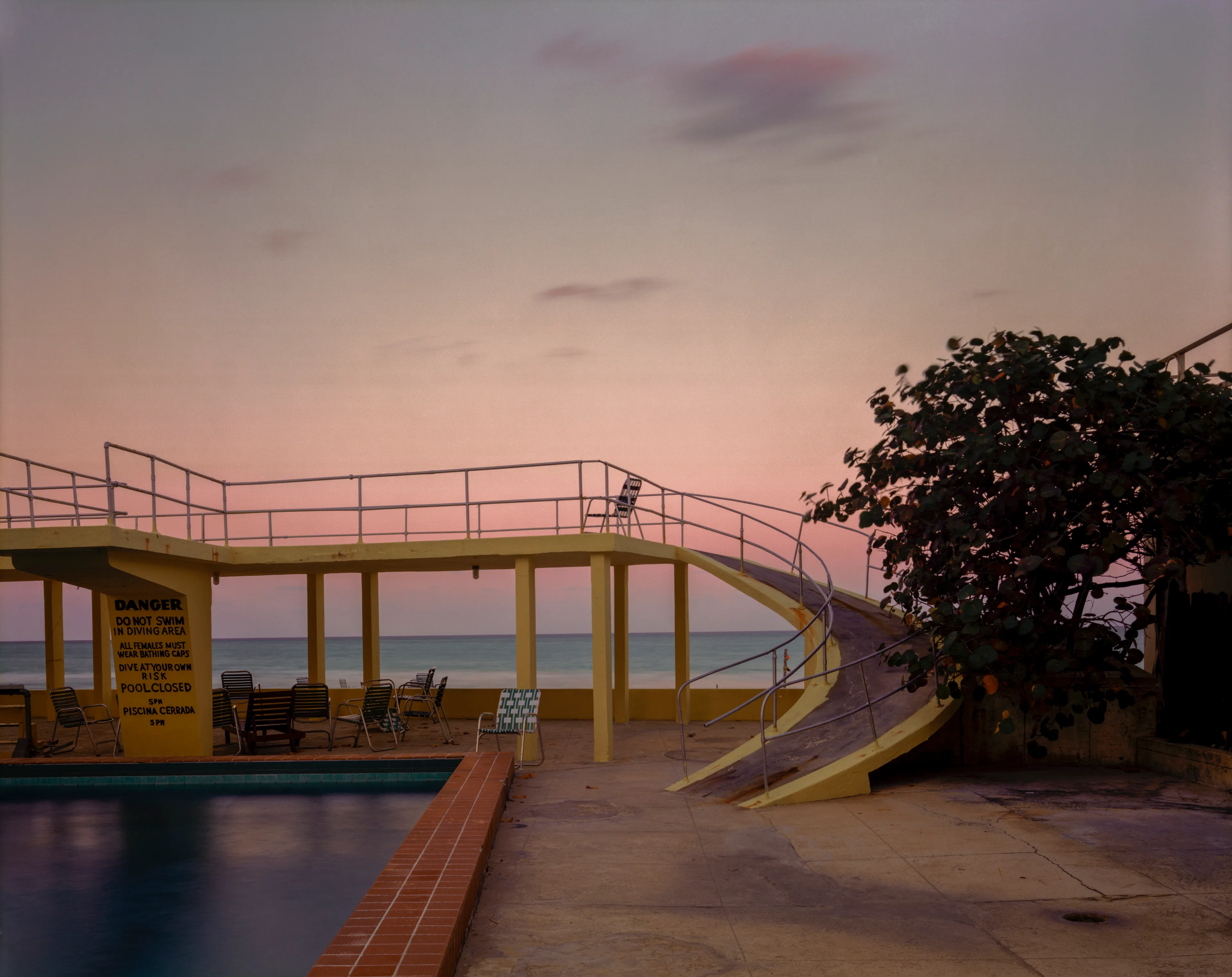 March 30, 1978: Yellow stair ramp, pool, sea Fort Lauderdale.

"I liked the sweep of the rising ramp taking one to the diving platform, with the sea below and the dusty pink sky above, and that lone chair where someone took a few minutes to contemplate the peace of the day". - Joel Meyerowitz.

Edition: 1 of 1