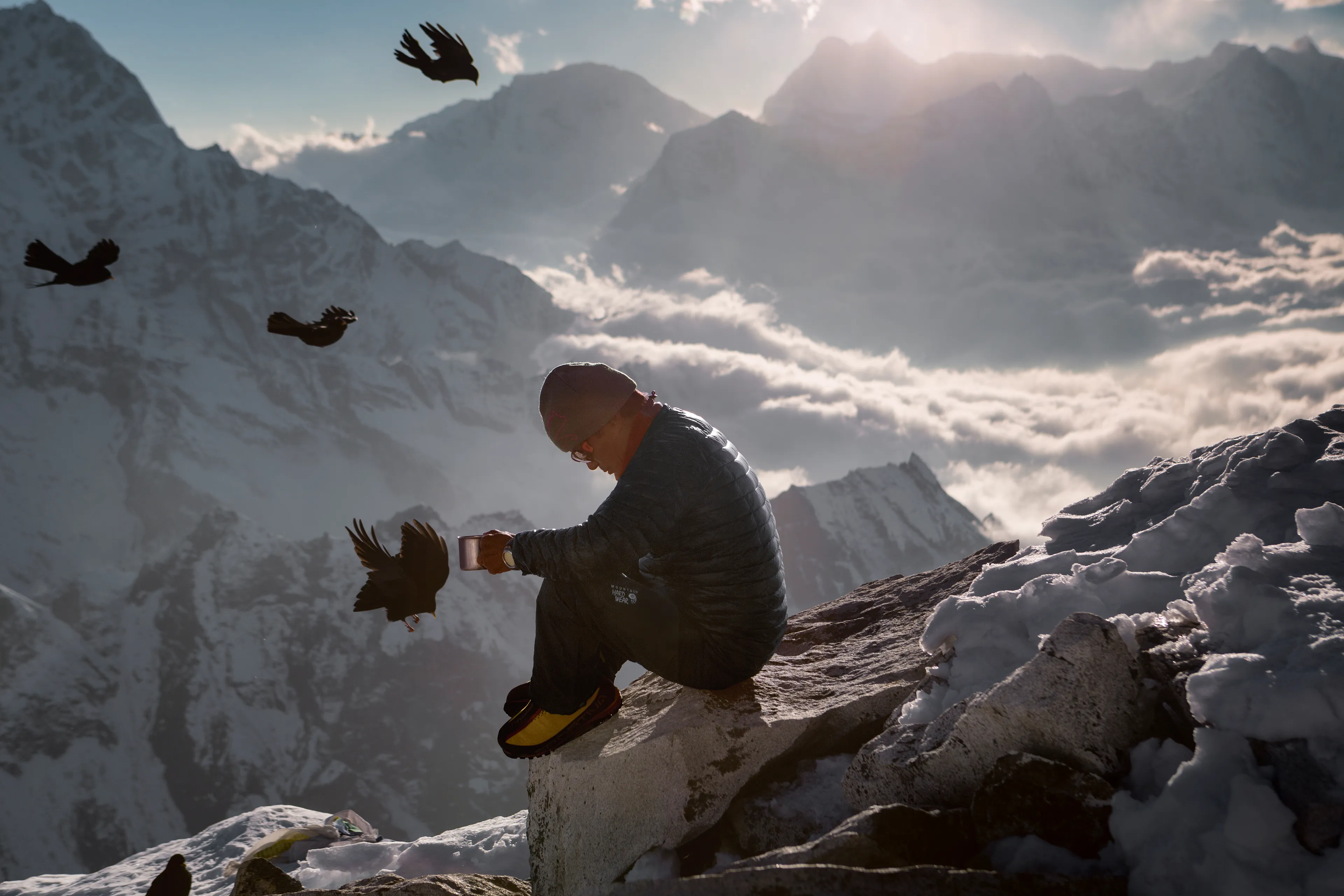 Ravens circling Lakpa Sherpa, who pauses for tea and a moment of reflection at Camp 1 on Ama Dablam (at 18,700ft /5,700m) in the Everest region of the Khumbu Valley.  This image was first published as the opening spread for a story called "Sorrow on the Mountain" in National Geographic Magazine in 2014.   

This was a special story for me spanning 90 days on assignment, over 3 trips and 16 months, living with the Sherpa community and traveling the Khumbu Region with them.  I knew I needed to get high-altitude climbing images of the Sherpas who worked on Everest helping westerners reach the summit, but my priority was to spend most of my time in the villages living with families and photographing daily life, culture, and spirituality away from the Everest Circus.  I didn’t want to risk my life on Everest in lines of hundreds of people (struggling up a mountain they shouldn't even be on), and I knew that nearby Ama Dablam was as, if not more, dramatic looking and would allow me more freedom to shoot without fear of death.  This camp above the clouds at Camp 1 was a special place and allowed me a look at how these elite climbers place the ropes up to the summits that make all the Western climber’s ascents possible.  

Sadly at the end of my assignment, before the story was set to be published, an avalanche above the Khumbu Icefall ended up killing 16 Sherpa climbers on the mountain.   The story about Sherpa Culture became the story of “Sorrow on the Mountain.”

https://www.nationalgeographic.com/magazine/article/mount-everest-avalanche-tragedy-sherpas

Photographed in 2013,  6300 x 4200px.  