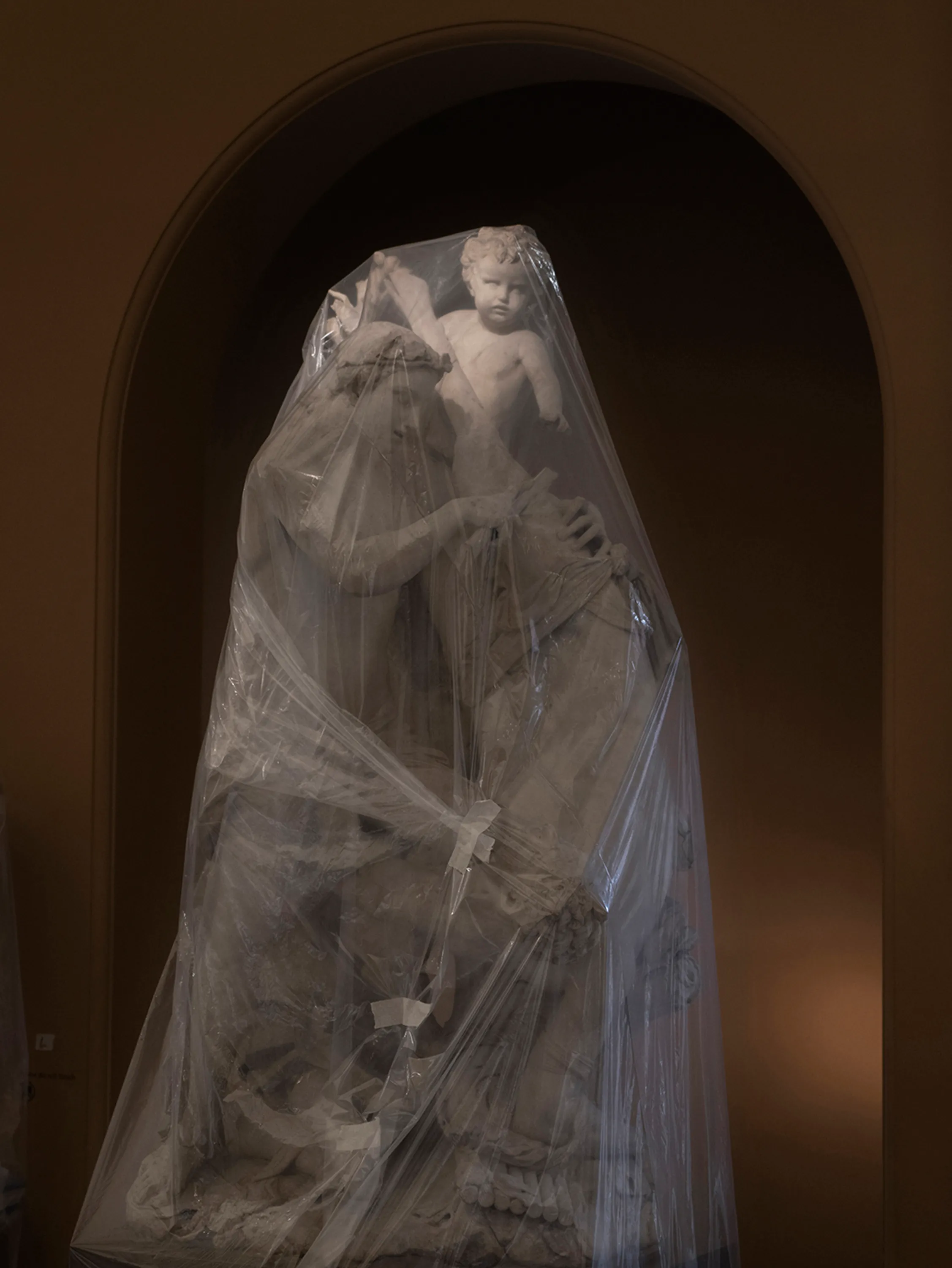 Assembly presents “Shrouded Sculptures” by UK based visual artist Simon Roberts. This NFT collection is a selection of photographs taken during the second Covid-19 lockdown whilst London’s Victoria and Albert Museum was closed to the public. These veiled statues, located in the Museum’s Dorothy and Michael Hintze Galleries, were covered for their protection during refurbishment and Roberts envisions them as a metaphor for our wider experience of the Covid-19 pandemic. The images speak of the extraordinary events of the past year, a global population suspended in time, restricted of movement and freedoms. We were forced to separate from one another, or if we were to meet, we were to hug through thick plastic sheeting, or wave through windows. The beauty of our world felt elusive, hidden beneath an entanglement of political mixed messages and misleading rhetoric. Unlike the statues of merchants, statesmen and traders, many of the sculptures in this gallery represent mythological or allegorical subjects. We see ancient mythology and 18th century neo-classicism meet 21st century plastic and gaffa tape, and the juxtaposition is eerie, disorientating and beautiful.

Simon Roberts is a visual artist based in the UK. Widely recognised for his large-format, tableaux photographs of the British landscape, his practice also encompasses video, text and installation work, which together, interrogate notions of identity and belonging, and the complex relationship between history, place and culture. His work has been exhibited nationally and internationally, and resides in major public and private collections, including the George Eastman House, Deutsche Börse Art Collection and Victoria & Albert Museum.