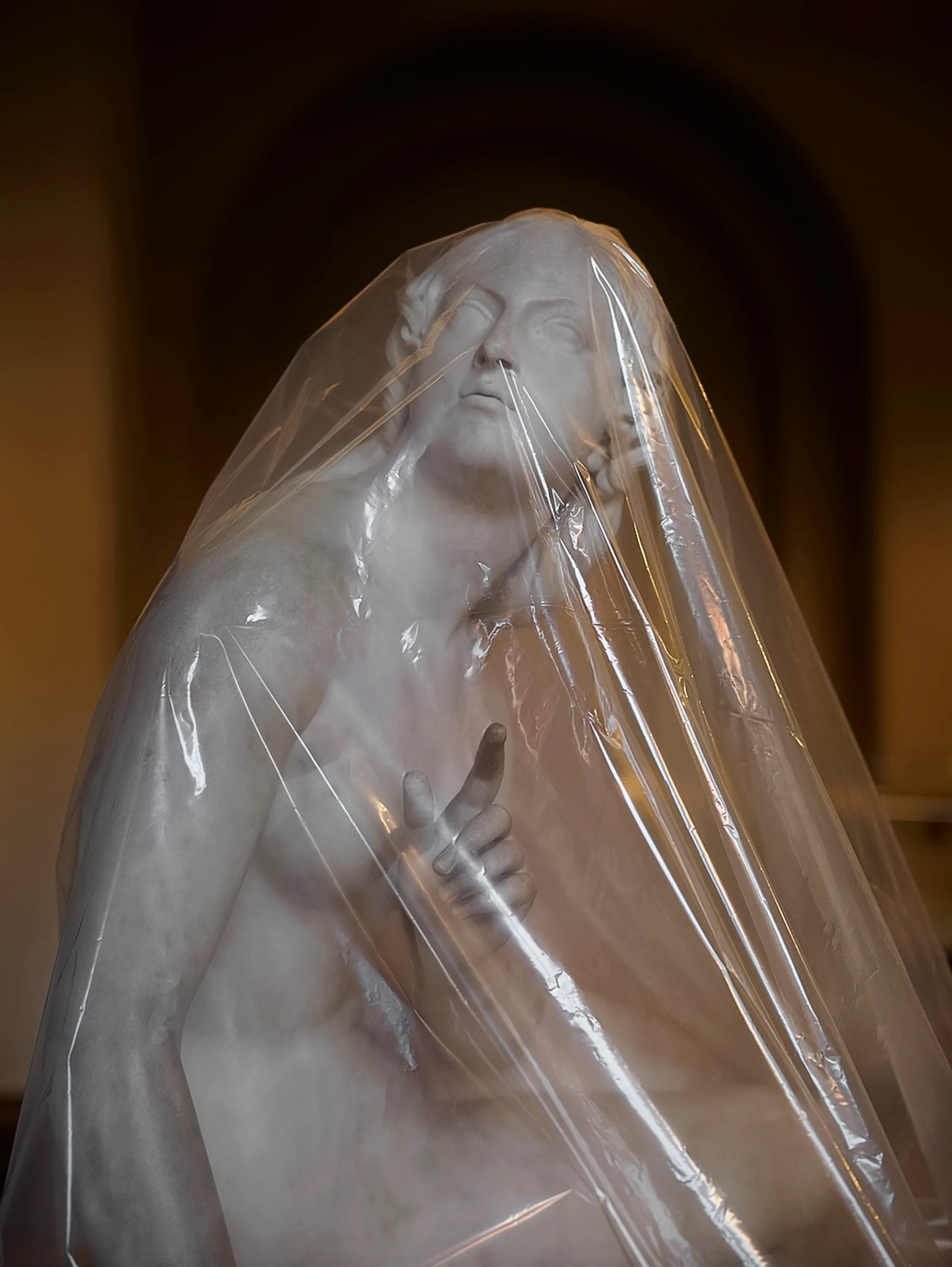 Assembly presents “Shrouded Sculptures” by UK based visual artist Simon Roberts. This NFT collection is a selection of photographs taken during the second Covid-19 lockdown whilst London’s Victoria and Albert Museum was closed to the public. These veiled statues, located in the Museum’s Dorothy and Michael Hintze Galleries, were covered for their protection during refurbishment and Roberts envisions them as a metaphor for our wider experience of the Covid-19 pandemic. The images speak of the extraordinary events of the past year, a global population suspended in time, restricted of movement and freedoms. We were forced to separate from one another, or if we were to meet, we were to hug through thick plastic sheeting, or wave through windows. The beauty of our world felt elusive, hidden beneath an entanglement of political mixed messages and misleading rhetoric. Unlike the statues of merchants, statesmen and traders, many of the sculptures in this gallery represent mythological or allegorical subjects. We see ancient mythology and 18th century neo-classicism meet 21st century plastic and gaffa tape, and the juxtaposition is eerie, disorientating and beautiful.

Simon Roberts is a visual artist based in the UK. Widely recognised for his large-format, tableaux photographs of the British landscape, his practice also encompasses video, text and installation work, which together, interrogate notions of identity and belonging, and the complex relationship between history, place and culture. His work has been exhibited nationally and internationally, and resides in major public and private collections, including the George Eastman House, Deutsche Börse Art Collection and Victoria & Albert Museum.