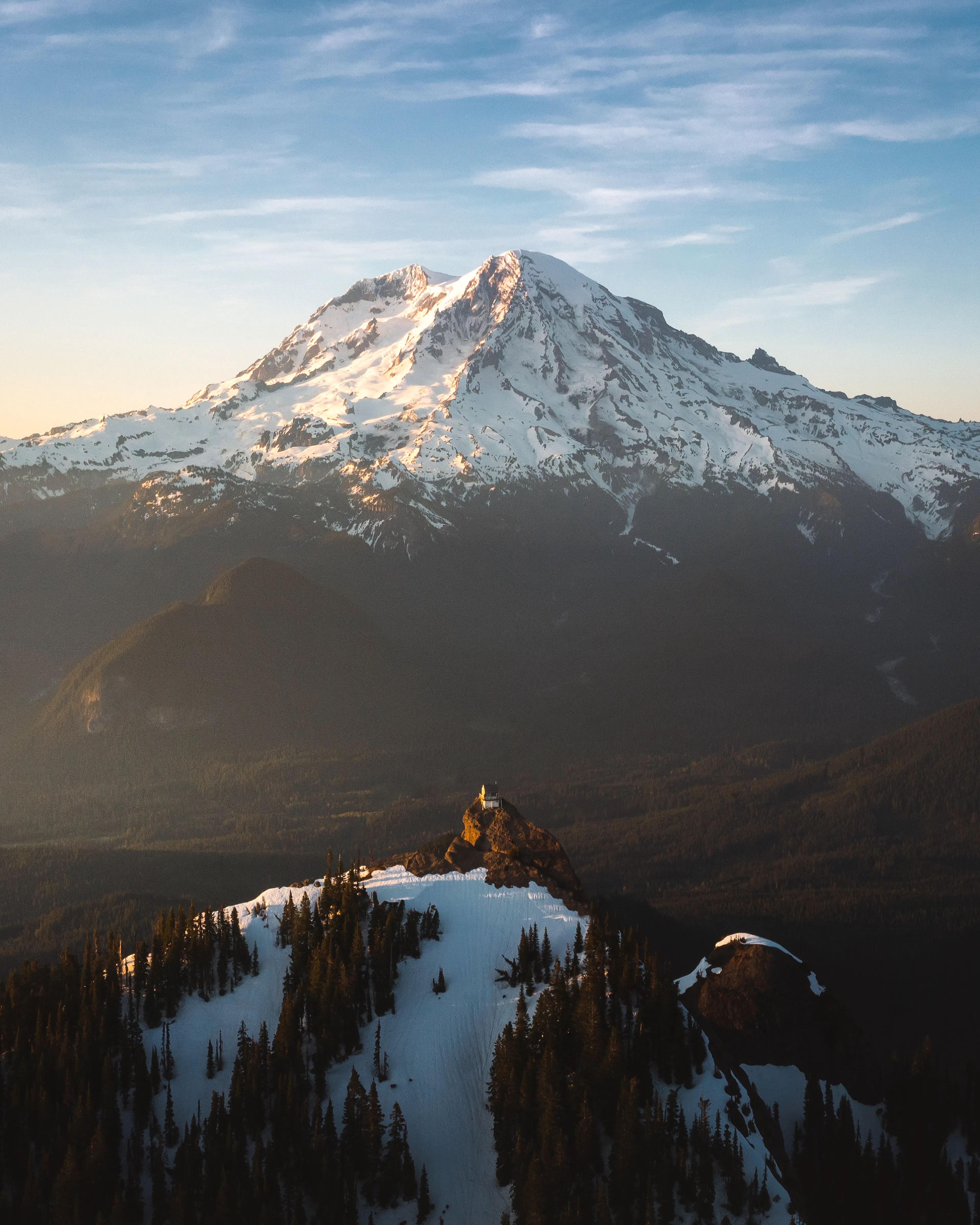 "Why live in the mountains when you could live on a mountain? Perched atop the peaks of the Washington mountains are dozens of standalone fire towers. These were used for years to monitor and report on new fires and monitor smoke, now they’re maintained as shelters for hikers, skiers and other mountain lovers. 

“The Mountain Hut” was captured at High Rock Lookout just south of Mount Rainier. I planned this piece for more than a year, even visiting twice only to have conditions not cooperate. In late spring 2021, I once again made the trek out and was welcomed by this scene and I finally captured a frame of the lookout lined up against the giant of the cascades.

Location: High Rock Lookout, Washington
Capture Date: May 15, 2021"