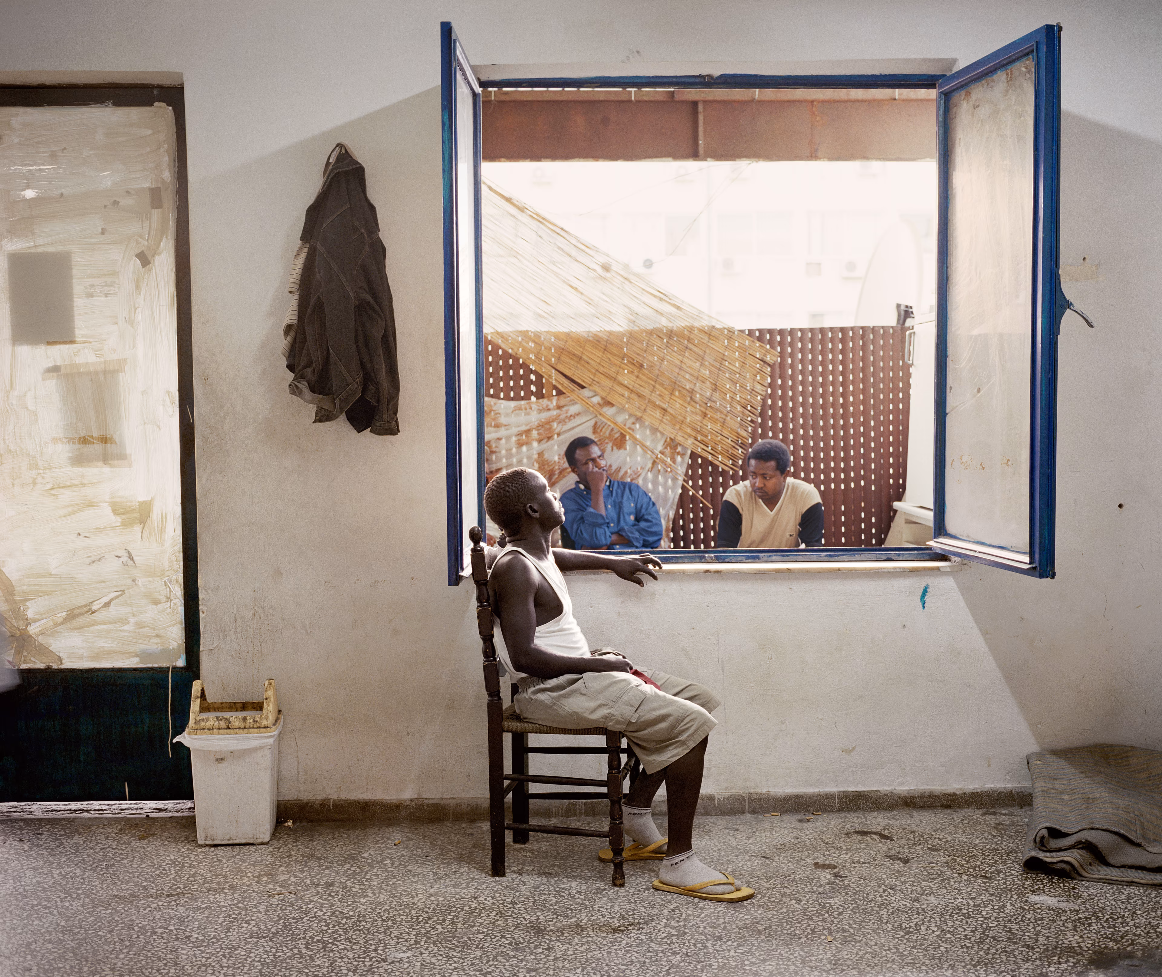 Magnum 75 #113 by Jim Goldberg. Athens, Greece. 2004  
A group of Sudanese refugees that live in a rundown, overcrowded, day-to-day tenement in Athens. They enjoy watching American television.

Magnum 75 is the inaugural NFT collection by Magnum Photos. Created in 2022 for the agency’s 75th anniversary year and released in three curations, the collection brings together 225 iconic images from Magnum photographers, taken across seven decades.

Each curation is composed in dialogue with a leading picture editor from across the globe and selected to embody the agency’s past, present, and future. This second curation was made in dialogue with Azu Nwagbogu, founder and director of African Artists’ Foundation and director of LagosPhoto Festival.

Nwagbogu says: “The vast Magnum archive reveals so much about the history of the modern world and its unresolved global issues with regard to ecology, humanity and technology. Rather than exploring Henri Cartier-Bresson’s ‘decisive moment,’ this collection studies the ‘indecisive moment’ — the interstitial spaces, the energized subjects floating in-between events, where little obvious action occurs but where the subject(s) seem to be caught in anticipation. Each image is charged with feeling, intent, foreboding, and meaning, composed with a sense of expectation that offers multiple scenarios and possibilities about past events. It is not revisionist history, but rather invites the collector and viewers to perhaps look at the image again, more closely.”

Edition: 1 of 1

© Jim Goldberg/Magnum Photos 2022 All Rights Reserved  
www.magnumphotos.com/terms-conditions/