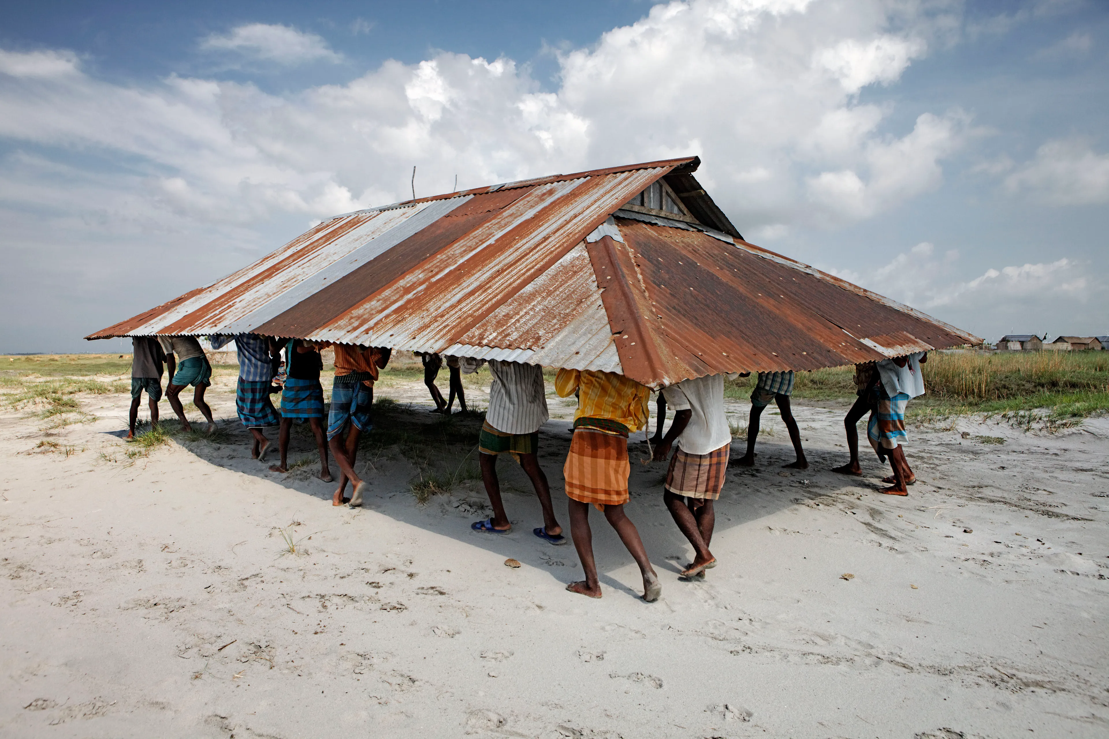 Magnum 75 #98 by Jonas Bendiksen. Kurigram District, Bangladesh. 2010  
Men moving the community mosque that was threatened by river erosion. In this flood-prone area, buildings are built to be able to be dismantled and moved in a single day.

Magnum 75 is the inaugural NFT collection by Magnum Photos. Created in 2022 for the agency’s 75th anniversary year and released in three curations, the collection brings together 225 iconic images from Magnum photographers, taken across seven decades.

Each curation is composed in dialogue with a leading picture editor from across the globe and selected to embody the agency’s past, present, and future. This second curation was made in dialogue with Azu Nwagbogu, founder and director of African Artists’ Foundation and director of LagosPhoto Festival.

Nwagbogu says: “The vast Magnum archive reveals so much about the history of the modern world and its unresolved global issues with regard to ecology, humanity and technology. Rather than exploring Henri Cartier-Bresson’s ‘decisive moment,’ this collection studies the ‘indecisive moment’ — the interstitial spaces, the energized subjects floating in-between events, where little obvious action occurs but where the subject(s) seem to be caught in anticipation. Each image is charged with feeling, intent, foreboding, and meaning, composed with a sense of expectation that offers multiple scenarios and possibilities about past events. It is not revisionist history, but rather invites the collector and viewers to perhaps look at the image again, more closely.”

Edition: 1 of 1

© Jonas Bendiksen/Magnum Photos 2022 All Rights Reserved  
www.magnumphotos.com/terms-conditions/