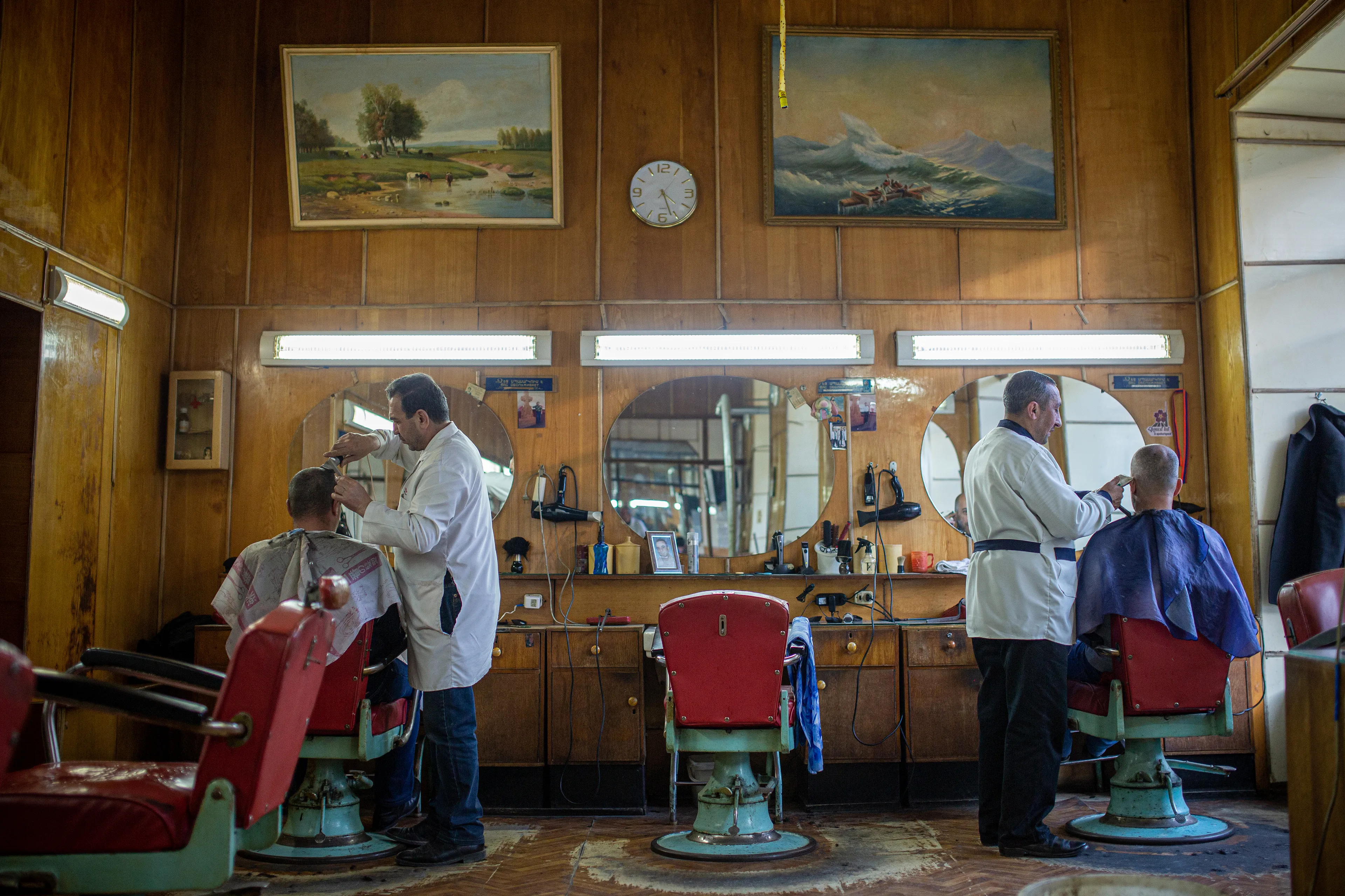 Inside the barbershop. Two barbers cutting clients’ hair.